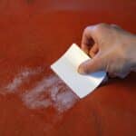 Picture of hand using plastic card to spread leather repair putty on scaly leather cushion