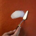 Picture of dry, scaly leather with hand using palette knife to apply white filler putty