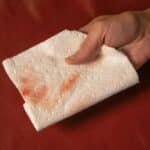 Picture of hand holding paper towel with transference, staining or crocking from red leather paint